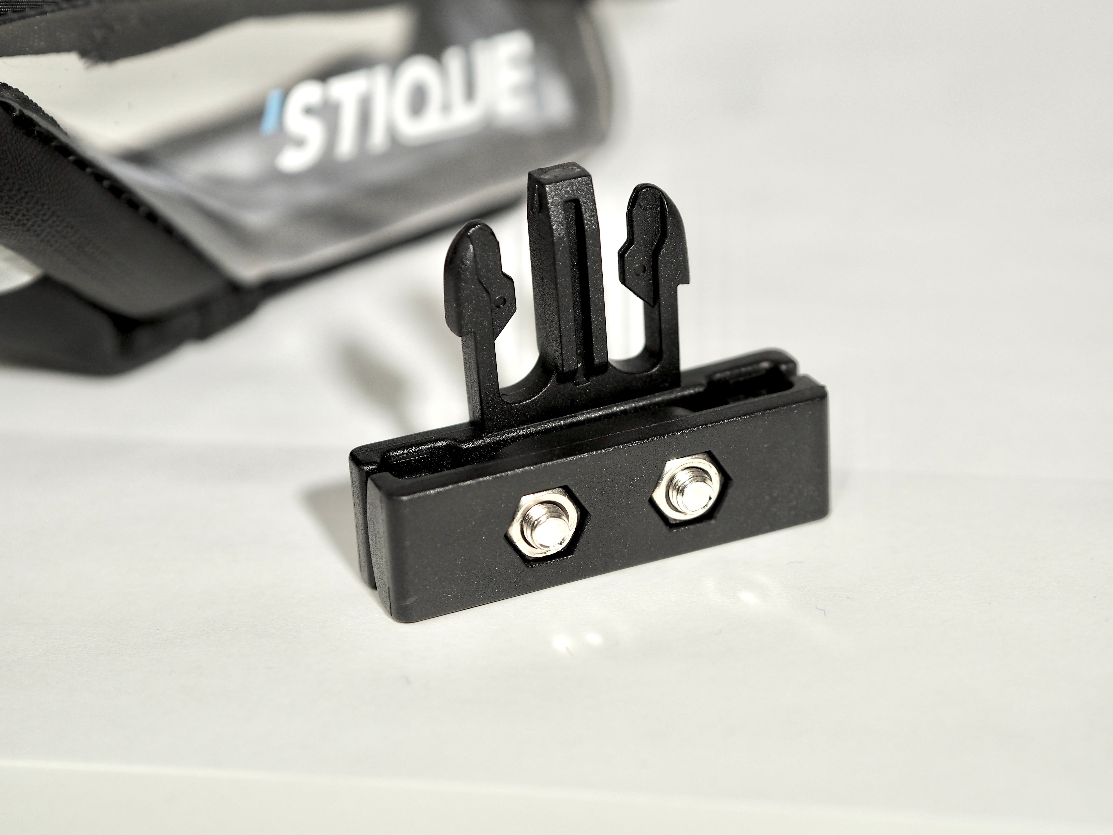 Close-up of Stique SaddleGuard mounting bracket with dual bolts, positioned in front of the saddle bag on a white surface